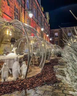 Terrasse abritée en verre avec tables élégamment dressées, entourée de décorations lumineuses.