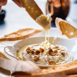 La brasserie propose un plat de fromage chaud avec des noisettes et des tranches de pain grillé.