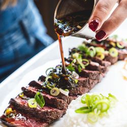 Un plat de viande tranchée avec une sauce, accompagné de riz et d'oignons verts.