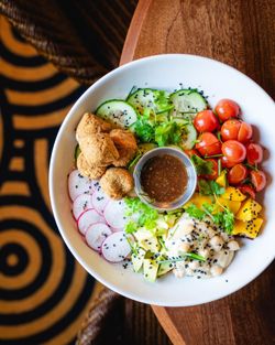 Salade composée maison avec tomates cerises, concombre, radis, avocat, falafels et sauce au centre.