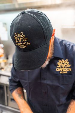 Employé portant une casquette et un uniforme bleu marine avec le logo Garden Ice Café, en cuisine.