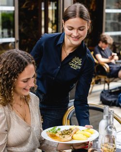Serveuse du Garden Ice Café servant un plat avec poisson et pommes de terre à une cliente en terrasse