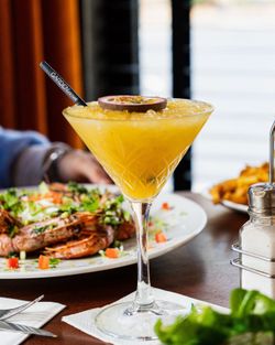 Un cocktail tropical servi dans un verre élégant, avec un plat de crevettes en arrière-plan.