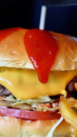Burger avec fromage fondu, tranche de tomate, laitue, sauce rouge et frites, présenté dans une brasserie à Brive-la-Gaillarde