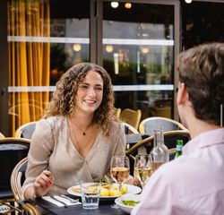 Terrasse de brasserie avec deux personnes dégustant un repas et du vin dans un cadre lumineux et convivial.
