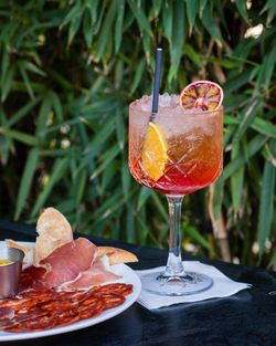 Cocktail coloré avec tranches d'orange accompagné d'une assiette de charcuterie sur une table en terrasse