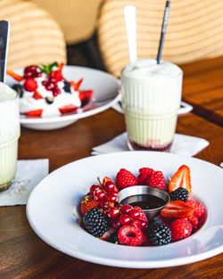 Assiette de fruits rouges frais avec sauce au centre, sur table en bois avec boissons et dessert flou en arrière-plan.