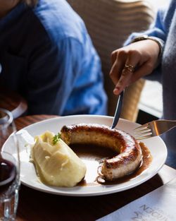 Saucisse et purée de pommes de terre avec sauce servies dans un restaurant, assiette blanche et fourchette en main.
