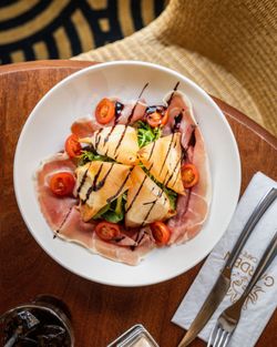 Assiette avec salade, tomates cerises, jambon cru et toasts nappés d'une sauce balsamique.