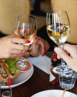 Deux personnes trinquent avec des verres de vin blanc et rosé à une table de restaurant avec des plats et condiments.