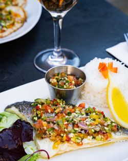 Plat de poisson garni de salsa fraîche et riz blanc, présenté sur une table avec un verre de vin.