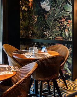 Coin repas avec table ronde et chaises en rotin dans une brasserie à ambiance tropicale et végétale.