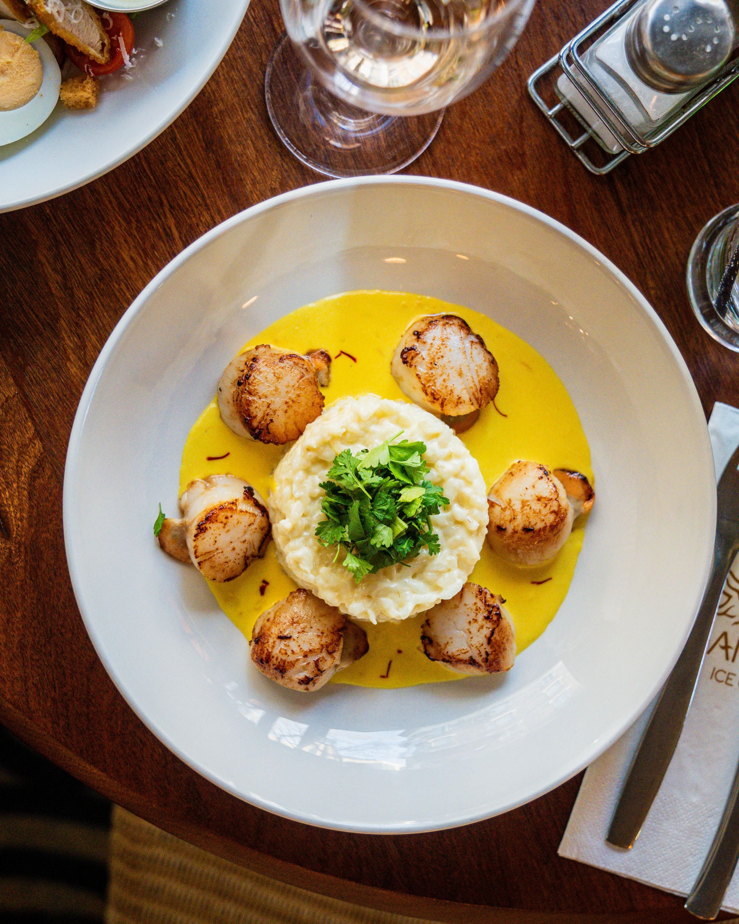 Noix de Saint-Jacques avec risotto crémeux, garnie de coriandre, dans un cadre chaleureux.