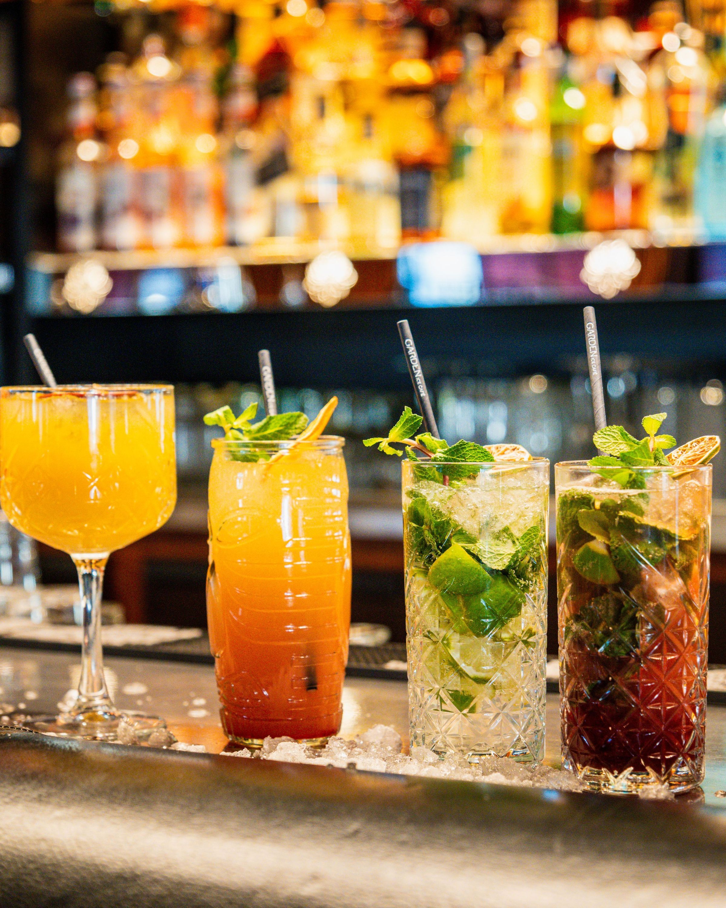 Cocktails variés avec herbes fraîches servis au bar d'une brasserie avec des bouteilles en arrière-plan.